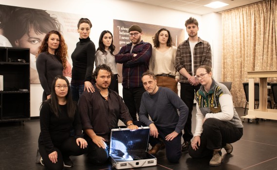 The HEIST team poses around an open briefcase in the rehearsal hall.